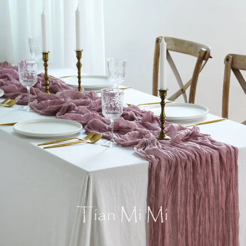 Une table élégante dressée avec des verres, des assiettes et des chandeliers, avec une nappe et un chemin de table roses, créant une ambiance chaleureuse et sophistiquée.