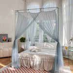 Lit à baldaquin avec rideaux éthérés dans une chambre lumineuse et spacieuse, avec un tapis à motif carrelé et des touches de décoration végétale.