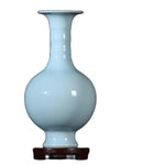 Vase en céramique de couleur bleu pâle sur un support en bois.