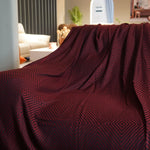 Cette image montre un plaid de couleur bordeaux décoré de motifs géométriques répétitifs en nuances de rouge, créant un effet élégant et sophistiqué dans un intérieur cosy.