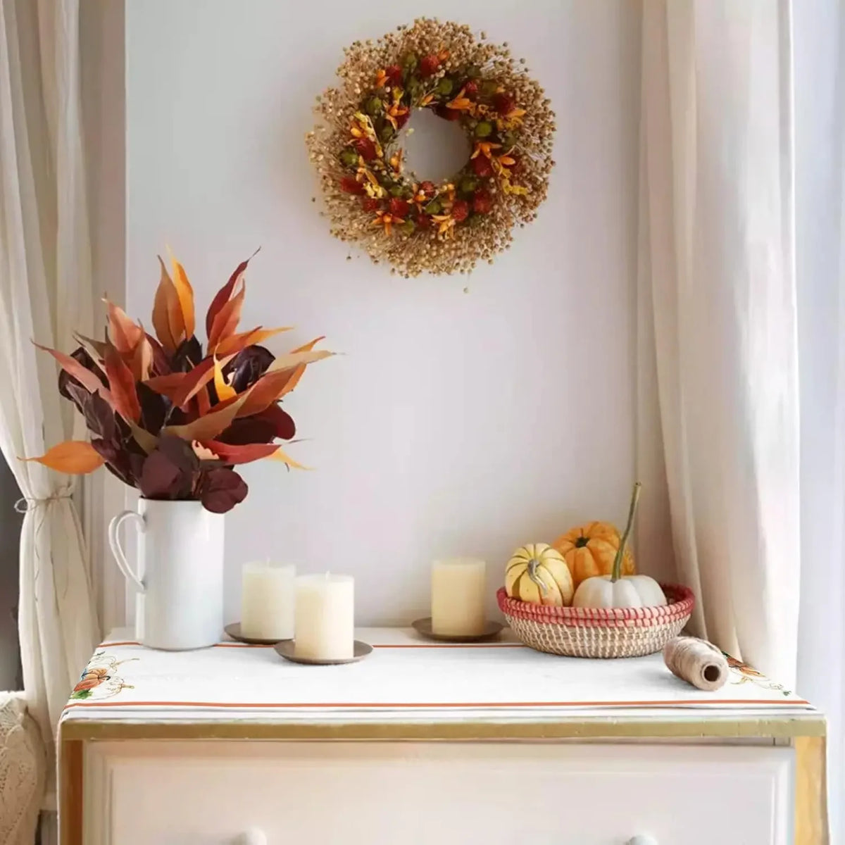 Un magnifique arrangement automnal composé d'une couronne décorative et d'un bouquet de fleurs ornés de cucurbitacées sur une commode blanche.