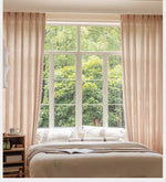 Voilage transparent marron clair en polyester dans une chambre lumineuse, encadrant une grande fenêtre donnant sur un jardin verdoyant.