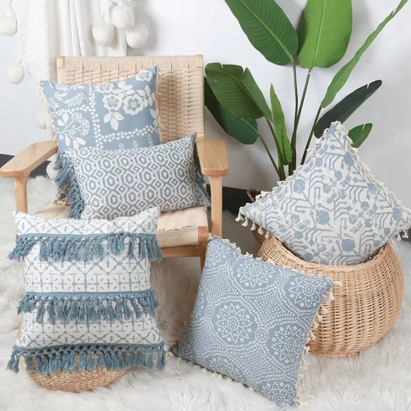Composition naturelle avec des coussins aux motifs élégants et un vase en osier sur un tapis blanc, avec des feuilles tropicales en arrière-plan.