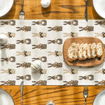 Sur une table en bois, on peut voir une assiette avec des tranches de pain et des ustensiles de cuisine, sur un fond décoré de motifs de bestioles en chocolat.