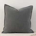 Coussin décoratif carré gris foncé avec des bords bien dessinés, créant une atmosphère chaleureuse et élégante dans un intérieur.