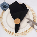 Élégante assiette blanche avec serviette de table noire, napperon tressé beige et décoration florale.