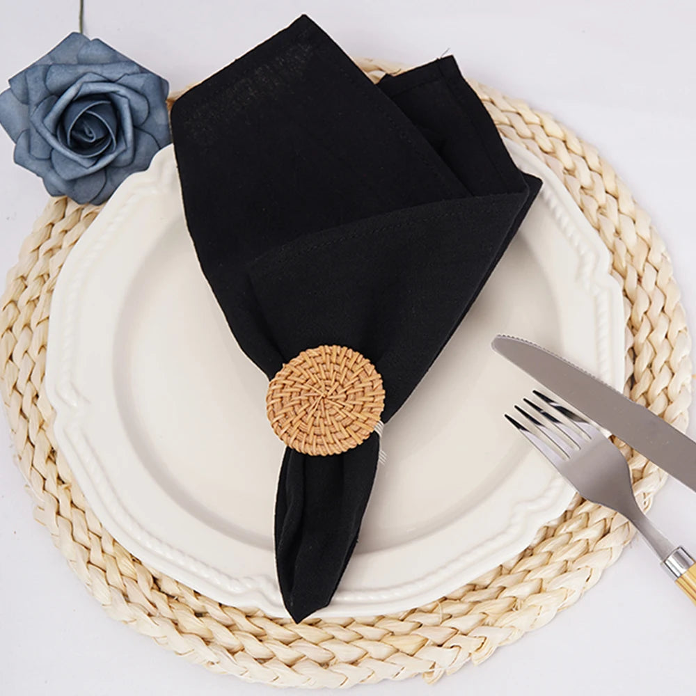 Nappes en fibres tressées avec une serviette noire pliée et maintenue par un élément décoratif en osier rond.