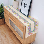 Sur le meuble en bois, un chemin de table coloré et floral ajoute une touche de design et de fraîcheur à l'espace.