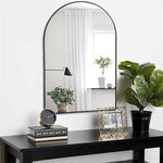 Élégante console noire avec grand miroir arqué, décorée de plantes vertes, de livres et d'un cadre photo.
