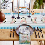 Cette image montre une belle table de salle à manger décorée avec des éléments thématiques de Pâques, notamment des figurines de lapins blancs et des accessoires de table coordonnés, créant une ambiance chaleureuse et festive pour un repas.