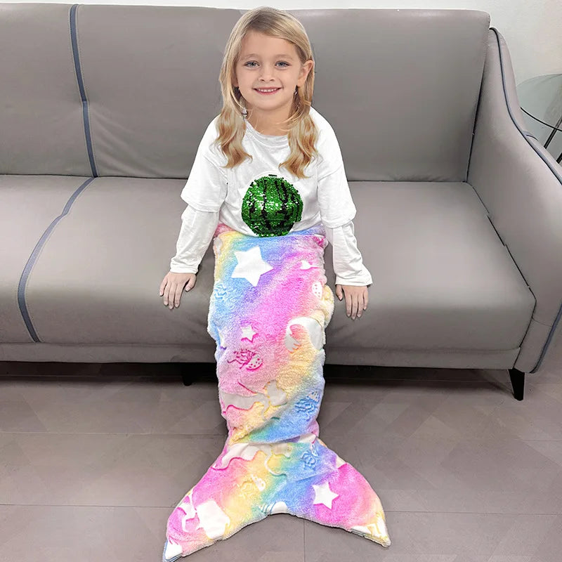 Une jeune fille souriante portant un t-shirt blanc et une jupe de sirène colorée, assise confortablement sur un canapé gris.