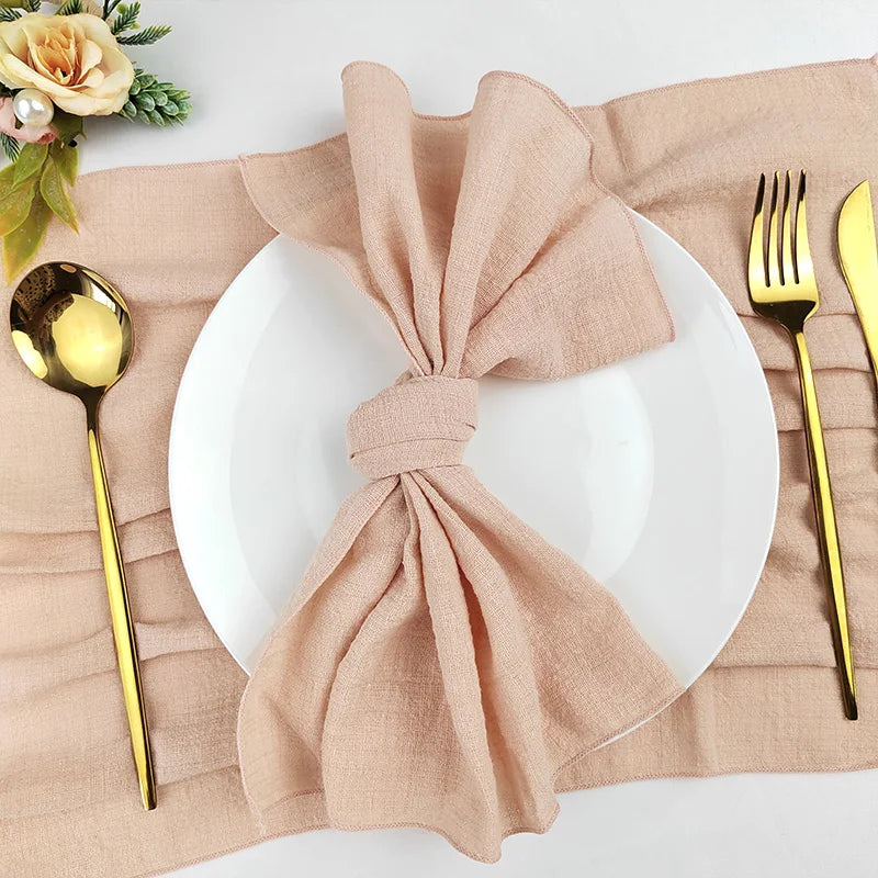 Une table de dîner élégante avec une serviette en lin beige nouée de manière décorative sur une assiette blanche, accompagnée de couverts dorés et d'une belle fleur.