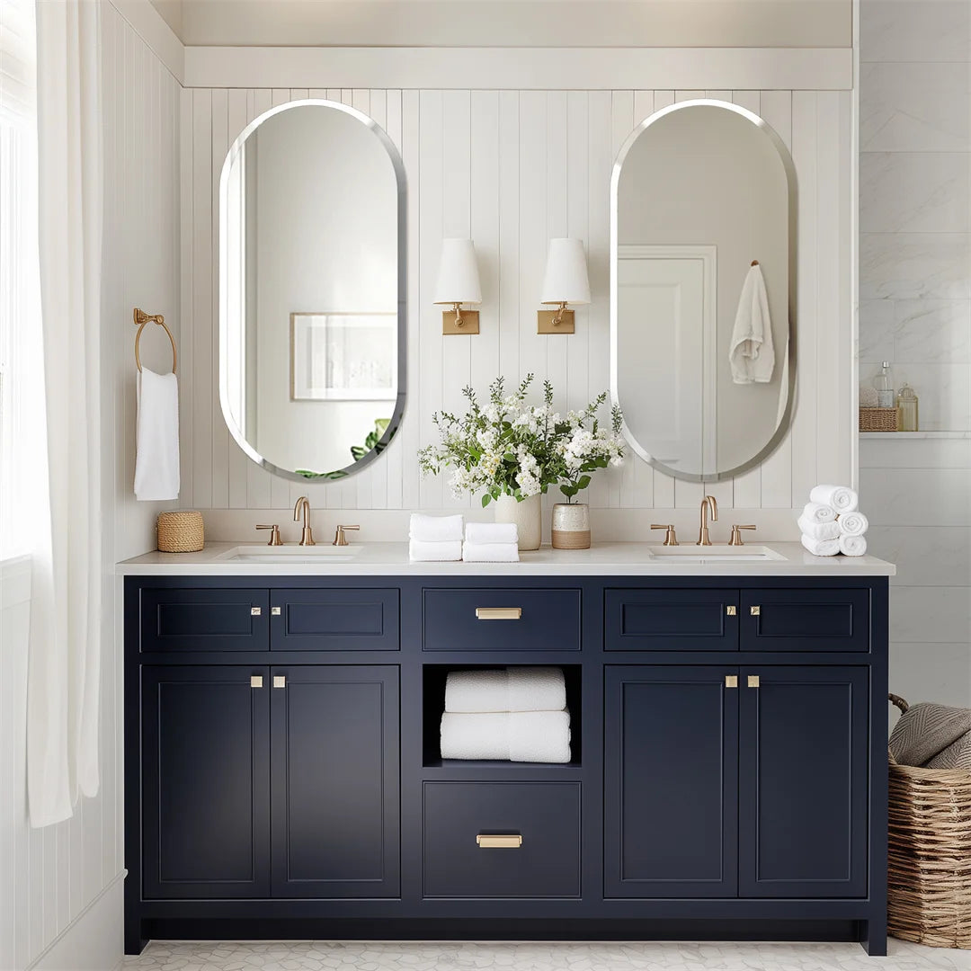 Une salle de bain épurée et élégante, avec des meubles noirs et des accents dorés, qui reflètent la lumière naturelle par le biais de grands miroirs ovales.