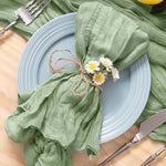 Une belle assiette bleue reposant sur une table en bois, accompagnée de couverts, d'un linge vert pomme orné de petites fleurs blanches et jaunes, créant une atmosphère chaleureuse et naturelle.