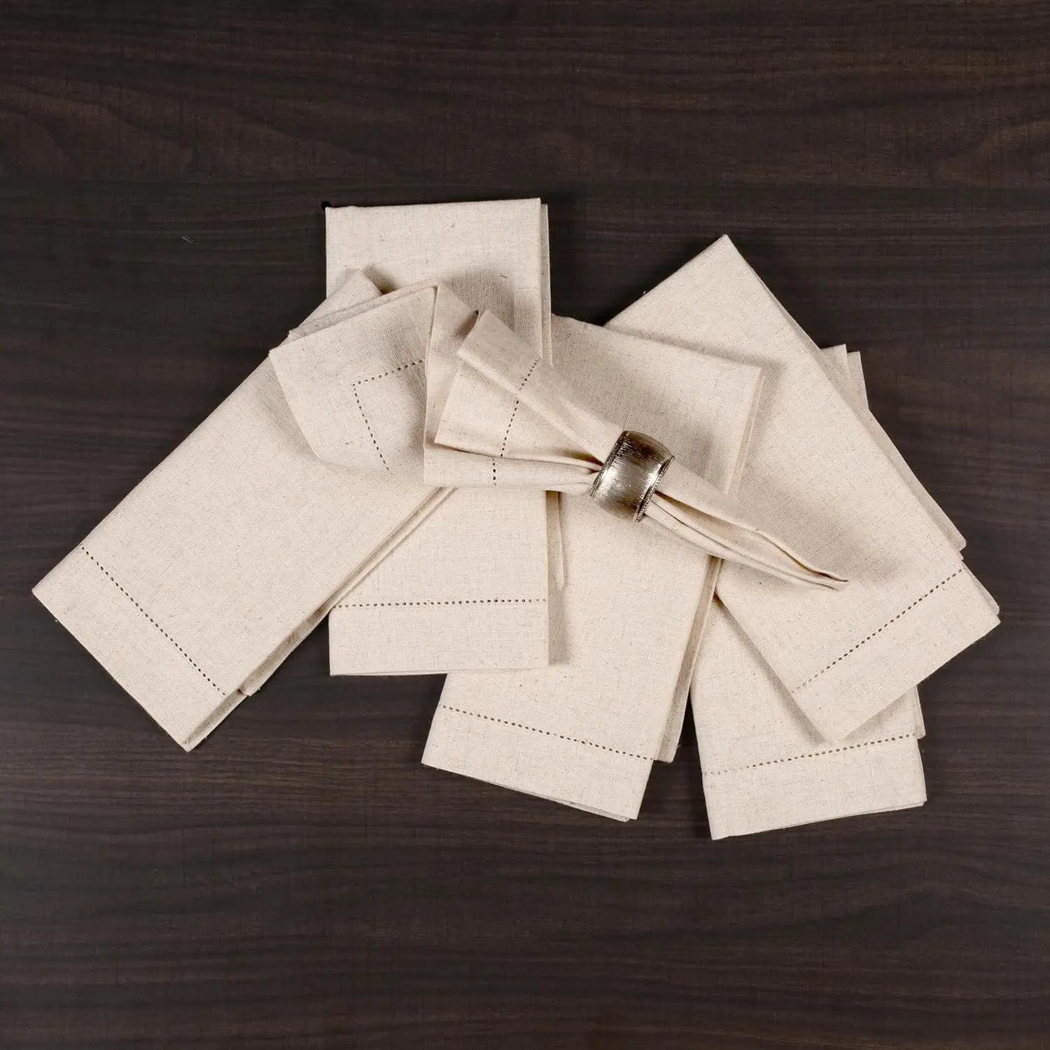 Des serviettes en lin blanc brodées de lignes et entouré d'un ruban blanc se trouvent sur une surface en bois sombre.