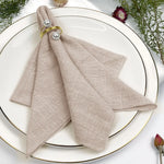 Une élégante serviette de table beige accompagnée d'anneaux dorés et d'accents végétaux, créant une décoration de table raffinée.