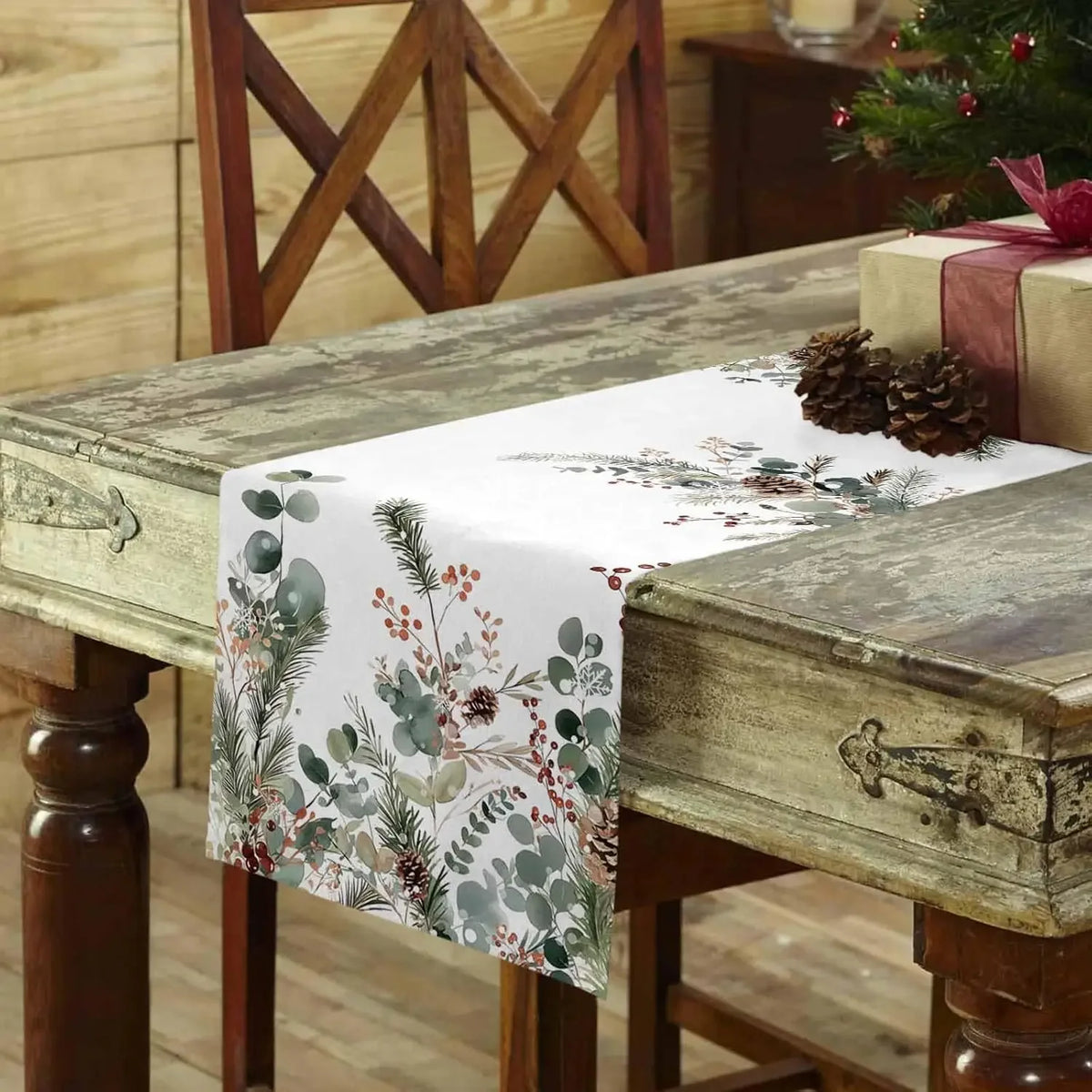 Un élégant chemin de table fleuri orné de cônes de pin et de décorations de Noël sur une table en bois vintage.