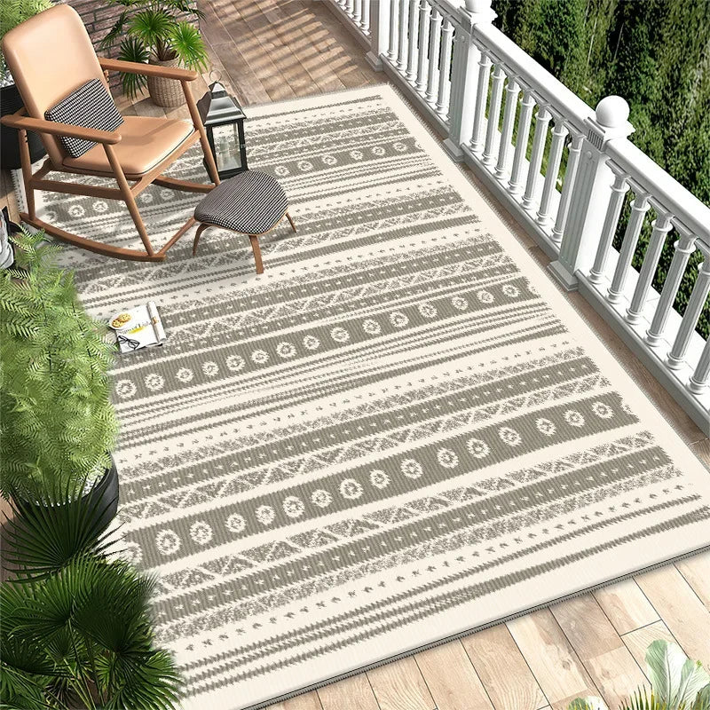 L'image montre un patio extérieur avec des meubles de jardin, un tapis à motifs graphiques et des plantes tropicales, créant une atmosphère décontractée et chaleureuse.