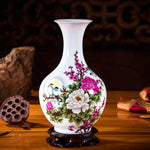 Vase décoratif en porcelaine blanche avec des fleurs de pivoine et d'autres fleurs asiatiques sur un piédestal en bois sombre.