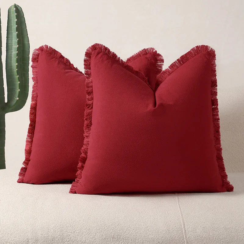 Deux élégants oreillers rouges avec des franges décoratives, sur un sol blanc, créant une atmosphère chaleureuse et élégante.