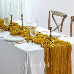 Une table avec une nappe blanche, des chandelles, des verres de cristal et un élégant chemin de table jaune en tissu froissé.