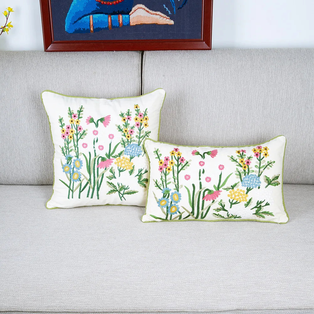 Deux oreillers décoratifs avec un motif fleuri coloré posés sur un canapé gris clair, avec une peinture murale en arrière-plan.