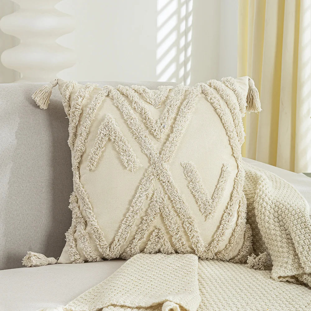 Coussin moelleux en blanc cassé orné de franges et de motifs graphiques décorant un canapé dans un intérieur lumineux.