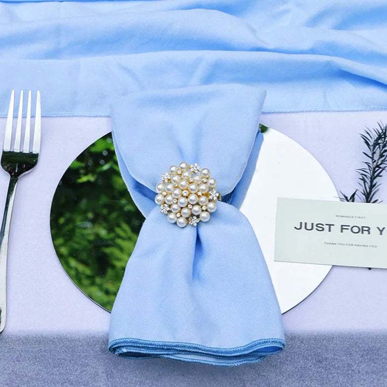 Une élégante serviette de table bleue, ornée d'un magnifique bouton de perles, posée sur un plateau avec une fourchette et un message de remerciement.