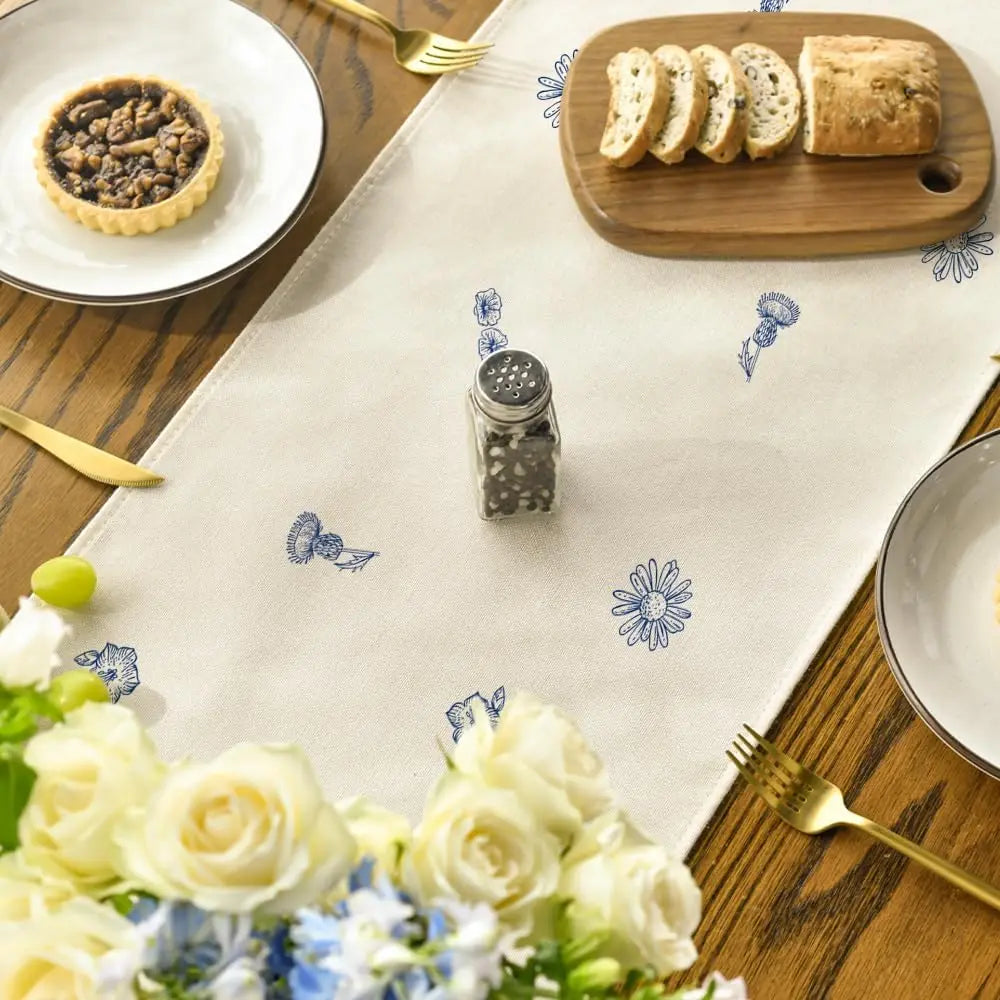 Une table dressée avec des fleurs fraîches, une tartelette et du pain tranchés, ainsi qu'un assortiment de condiments et de couverts, créant une ambiance chaleureuse et accueillante.