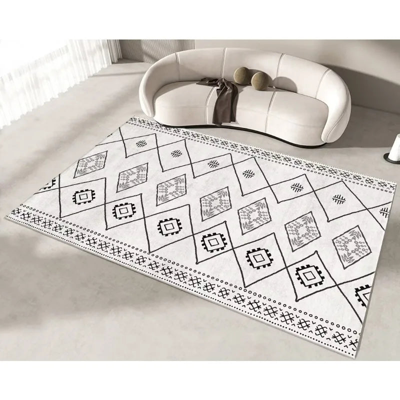 Tapis rectangulaire en noir et blanc aux motifs géométriques tribaux, posé sur le sol près d'un fauteuil blanc dans un intérieur lumineux.