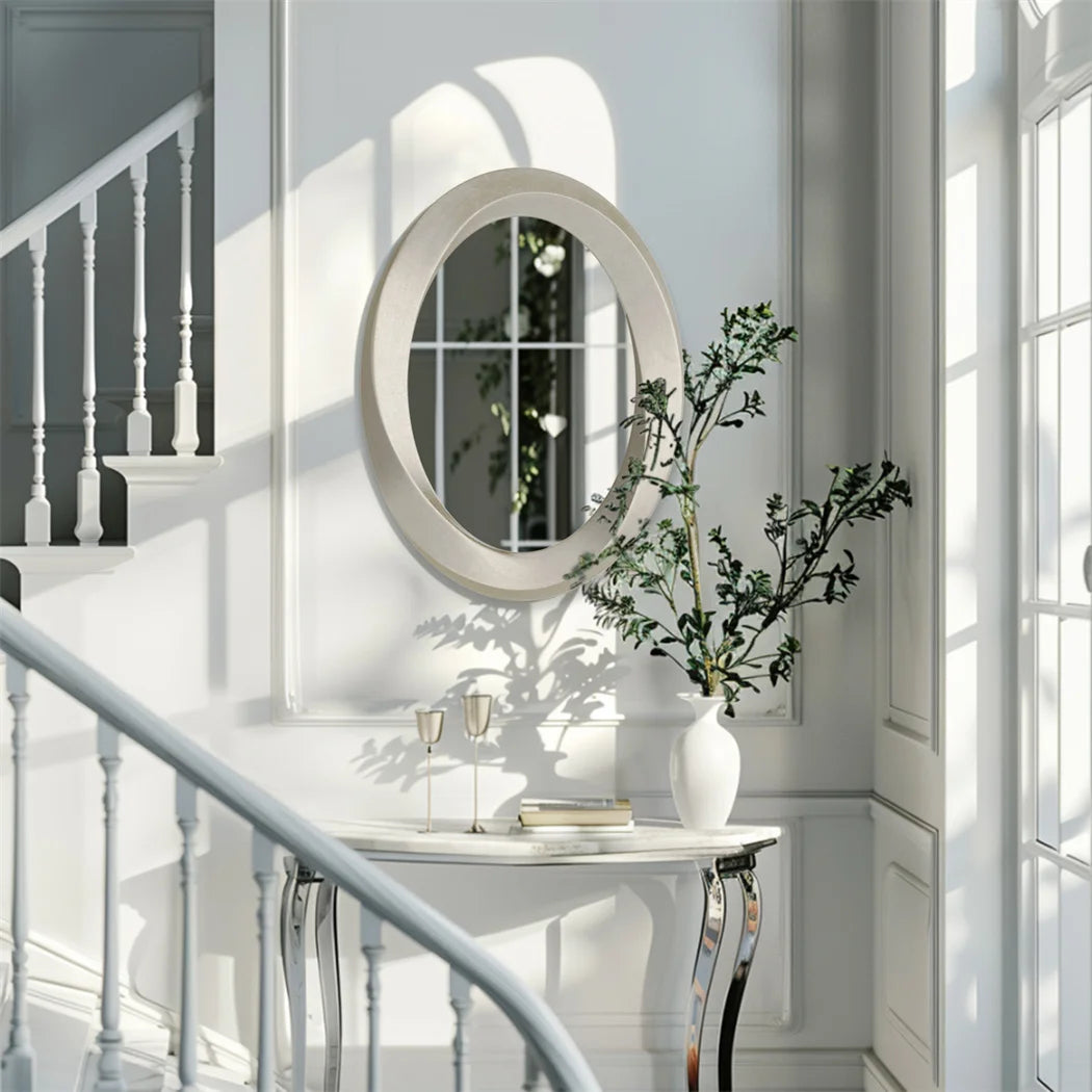 Un intérieur élégant avec un miroir ovale, une console en marbre et une plante décorative près d'une fenêtre baignée de lumière.