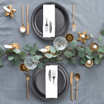 Élégante table de fête avec des assiettes noires, des couverts dorés, des bougies et une décoration végétale.