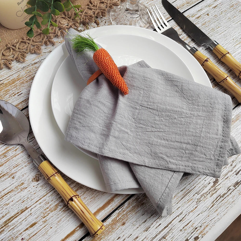 Assiette blanche sur une table en bois avec serviette grise et cuillère, fourchette et couteau en bambou, décorée avec une plante succulente et une carotte ornementale.