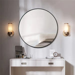 Une salle de bain élégante avec un miroir rond, des appliques murales et un meuble bas blanc avec des tiroirs.