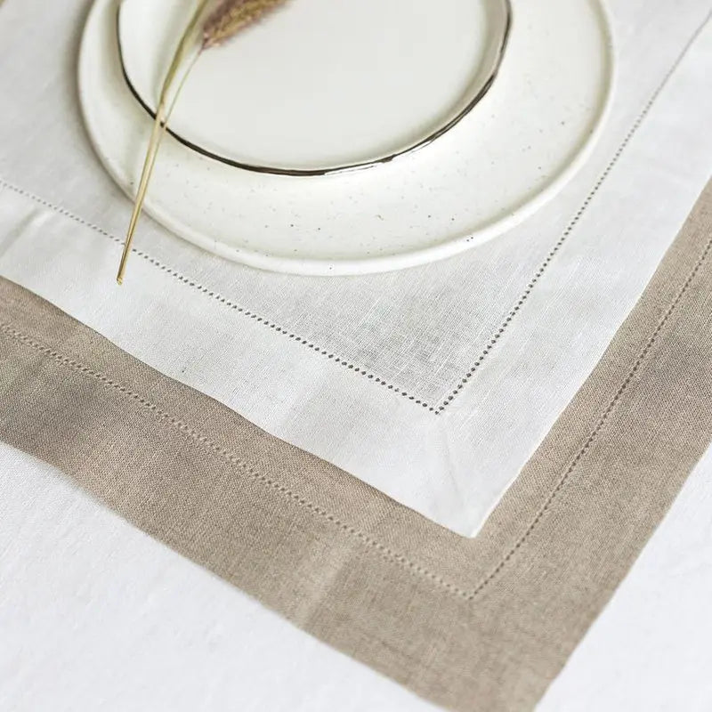 Des assiettes et des couverts disposés sur une nappe de linge blanc et beige, reflétant une ambiance élégante et raffinée.