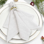 Serviette blanche élégamment disposée sur une assiette blanche avec des anneaux dorés et des fleurs décoratives.