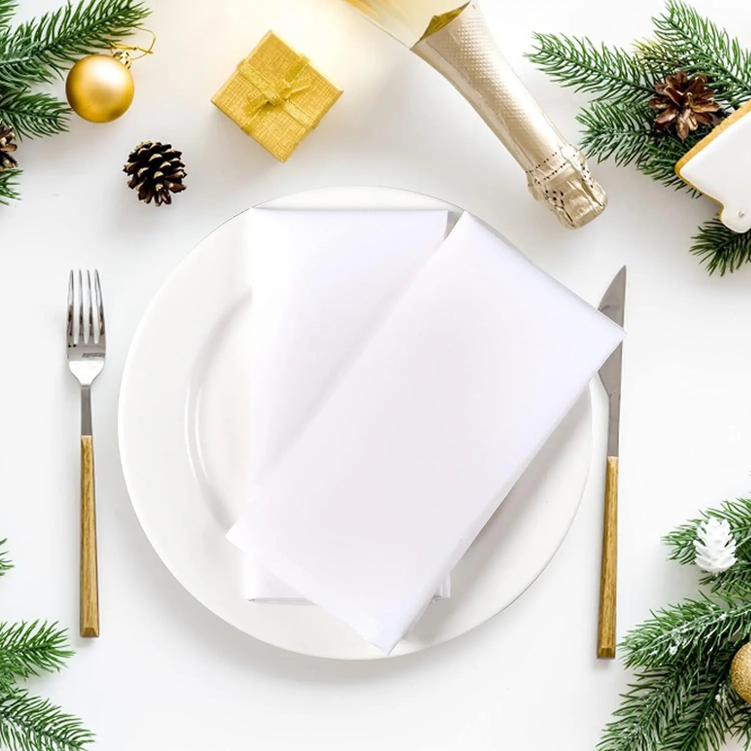 Assiette blanche avec couverts dorés, entourée de décorations de Noël vertes et dorées sur fond blanc.