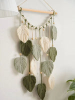 Décoration murale suspendue avec de belles feuilles en macramé et perles en bois, créant une ambiance apaisante et naturelle dans la pièce.