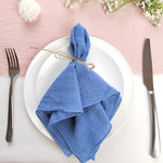 Une serviette en tissu bleu, délicatement pliée et attachée avec de la corde, décorée de fleurs blanches sur un fond rose pastel.