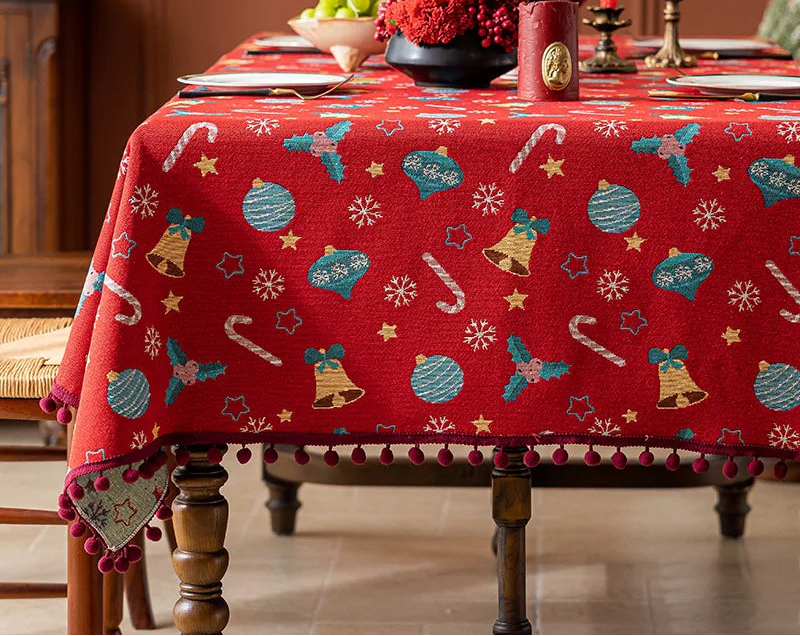 Une magnifique nappe de table rouge ornée de motifs de Noël colorés, comme des boules, des cloches et des flocons de neige, créant une ambiance festive et chaleureuse pour les fêtes.