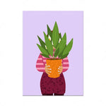 Une personne debout tenant dans ses mains un pot de plantes tropicales avec de grandes feuilles vertes.