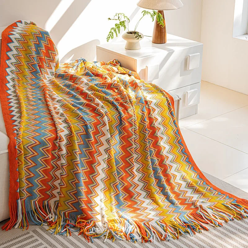Une couverture multicolore aux motifs géométriques audacieux et éclatants, ornée de franges, confère une ambiance chaleureuse et accueillante à cette pièce de décoration.
