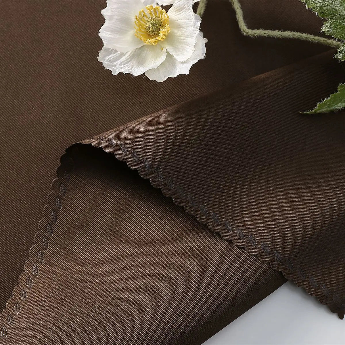 Une magnifique fleur blanche épanouie se détache sur un tissu sombre texturé, créant une belle composition contrastée.