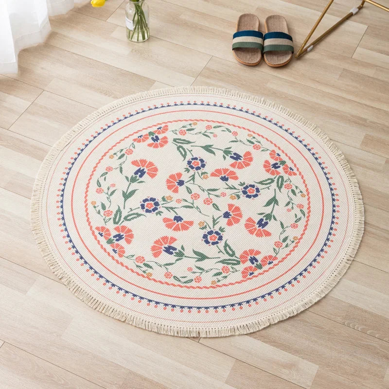 Un tapis rond orné de motifs floraux colorés, posé sur un sol en bois clair avec des sandales en tricot à proximité.