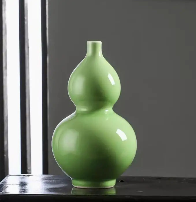 Vase en forme de gourde de couleur verte brillante placé sur un rebord près d'une fenêtre sombre.