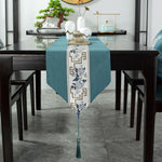 Une élégante chemin de table vert turquoise avec un motif floral bleu et blanc, sur une table en bois sombre avec des décorations asiatiques.