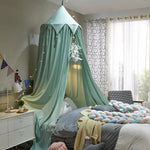 Chambre d'enfant confortable et aménagée avec des couleurs et des textures douces, un lit avec un baldaquin en forme de pyramide et des oreillers multicolores.