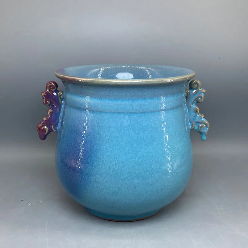 Un pot en céramique bleu clair avec des ornements dorés et des poignées violettes, offrant un bel objet décoratif de style vintage.