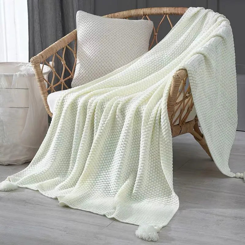 Couverture confortable tricotée en blanc étendue sur un fauteuil en rotin, créant une atmosphère cocooning dans la pièce.