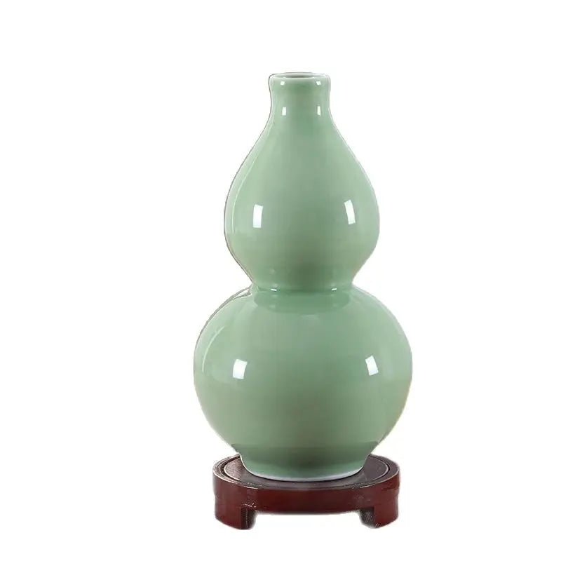 Vase décoratif en céramique vert pastel avec un motif de forme de gourde, posé sur un support en bois.